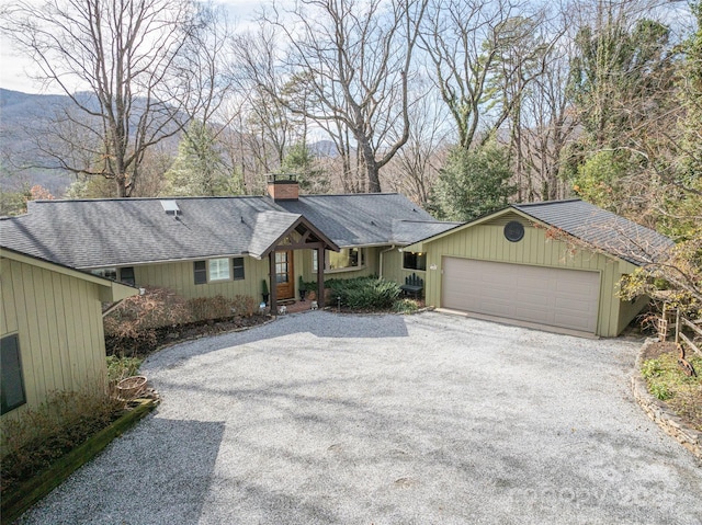 ranch-style house with a shingled roof, a mountain view, a chimney, and gravel driveway