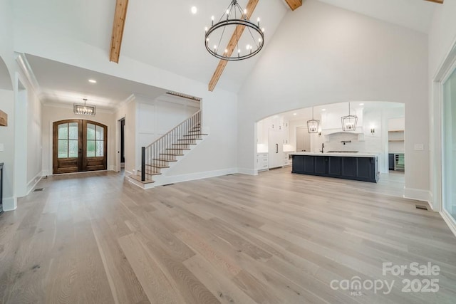 unfurnished living room featuring light hardwood / wood-style flooring, a notable chandelier, beam ceiling, and french doors