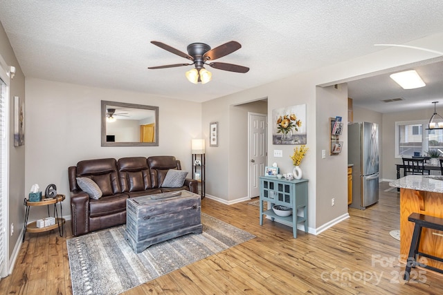 living room with ceiling fan with notable chandelier, light hardwood / wood-style flooring, and a textured ceiling