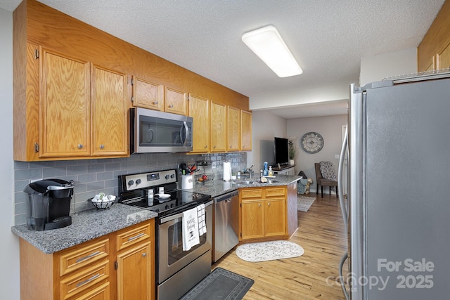 kitchen featuring sink, dark stone counters, light hardwood / wood-style floors, kitchen peninsula, and stainless steel appliances