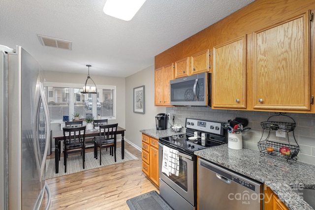 kitchen with tasteful backsplash, appliances with stainless steel finishes, light stone countertops, and light hardwood / wood-style floors