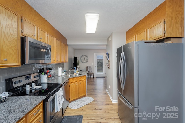 kitchen with sink, a textured ceiling, light hardwood / wood-style flooring, stainless steel appliances, and decorative backsplash