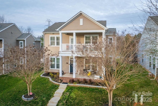 traditional-style home with a balcony, a shingled roof, a porch, and a front yard