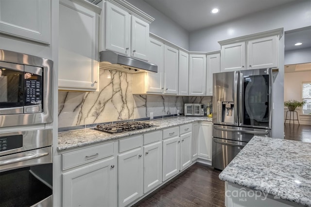 kitchen featuring dark wood finished floors, appliances with stainless steel finishes, light stone counters, under cabinet range hood, and white cabinetry