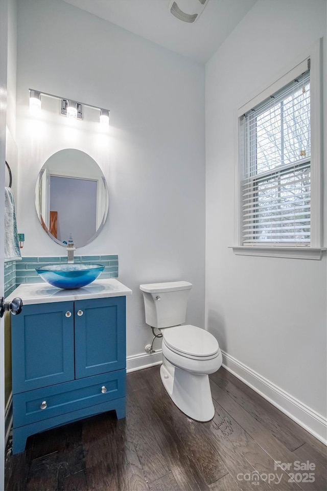 half bath featuring baseboards, vanity, toilet, and wood finished floors