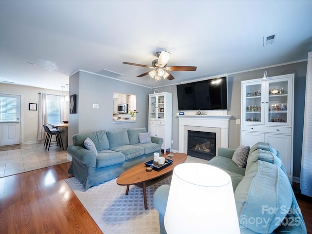 living room with ornamental molding, ceiling fan, and light wood-type flooring