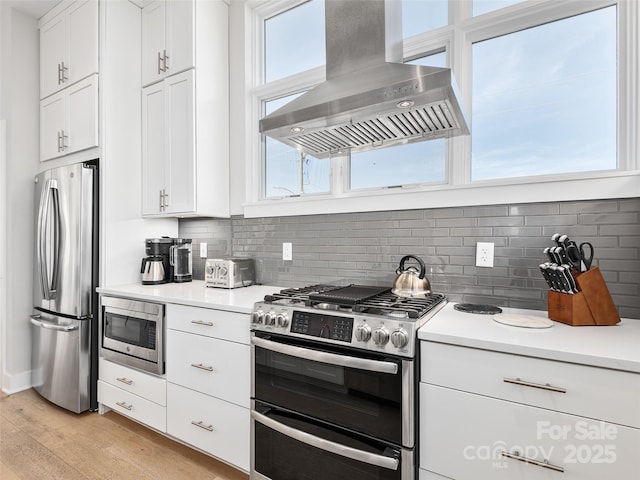 kitchen with white cabinetry, backsplash, stainless steel appliances, light hardwood / wood-style floors, and island exhaust hood