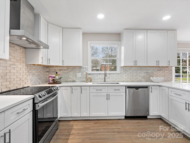 kitchen featuring wall chimney range hood, electric stove, white cabinetry, and stainless steel dishwasher