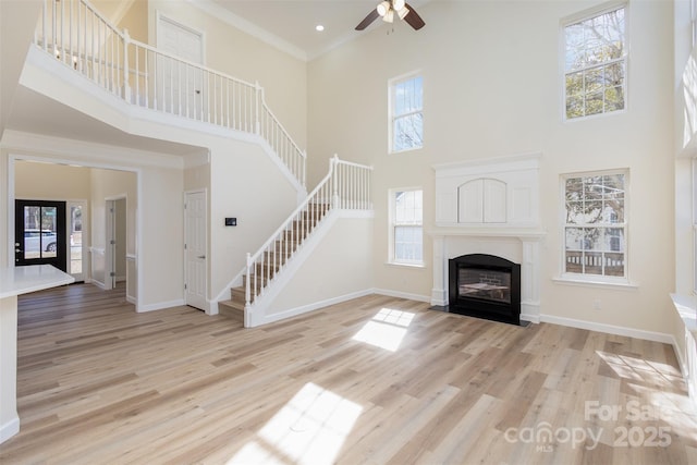 unfurnished living room with a high ceiling, crown molding, ceiling fan, and light hardwood / wood-style floors