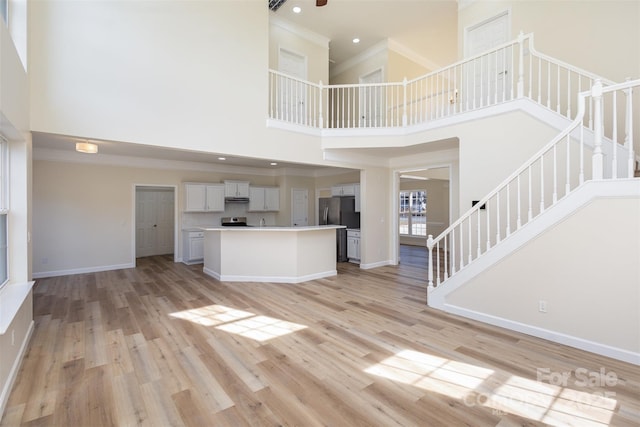 unfurnished living room featuring a high ceiling, ornamental molding, and light hardwood / wood-style flooring