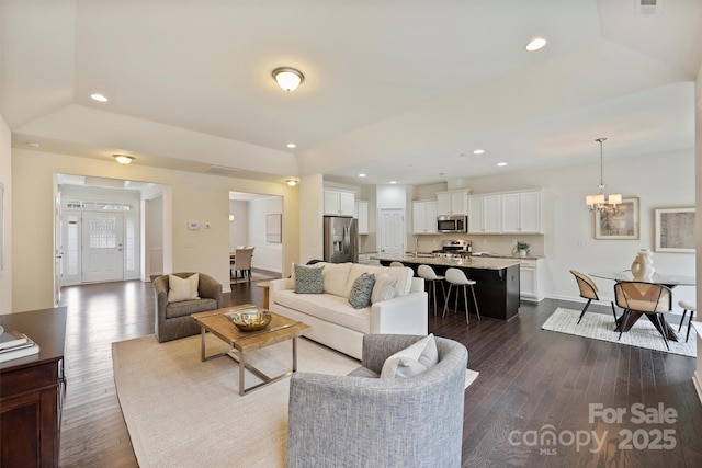 living room with an inviting chandelier, dark hardwood / wood-style flooring, and a raised ceiling