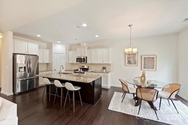 kitchen with white cabinetry, an island with sink, pendant lighting, stainless steel appliances, and light stone countertops