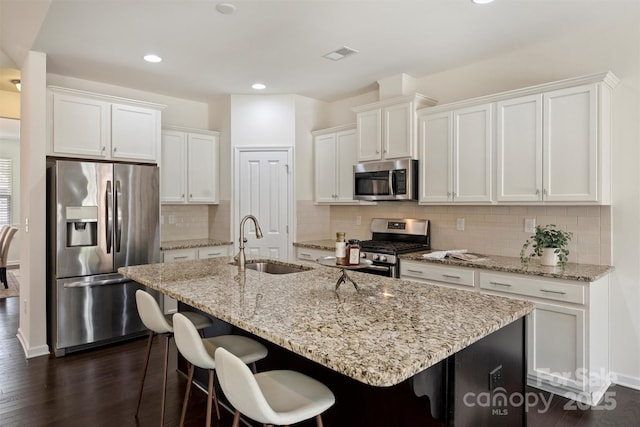 kitchen with sink, white cabinetry, appliances with stainless steel finishes, dark hardwood / wood-style floors, and an island with sink