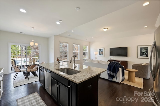 kitchen featuring sink, light stone counters, appliances with stainless steel finishes, pendant lighting, and a kitchen island with sink