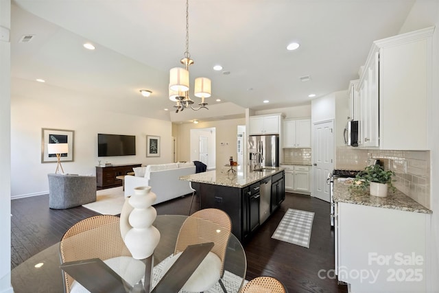 kitchen featuring pendant lighting, appliances with stainless steel finishes, a kitchen island with sink, backsplash, and white cabinetry