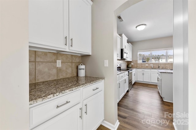 kitchen featuring appliances with stainless steel finishes, backsplash, dark hardwood / wood-style floors, light stone countertops, and white cabinets