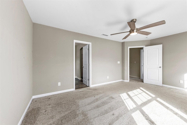 unfurnished bedroom featuring dark colored carpet, ensuite bathroom, and ceiling fan