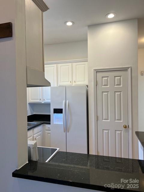 kitchen with dark stone counters, range, refrigerator with ice dispenser, and white cabinets