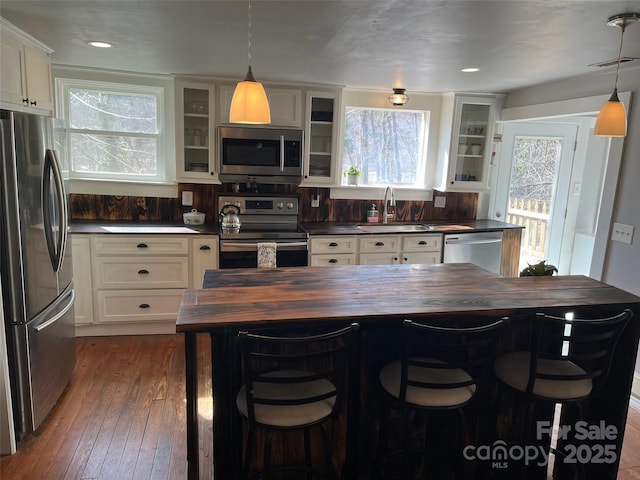 kitchen with appliances with stainless steel finishes, wooden counters, white cabinets, sink, and a kitchen bar