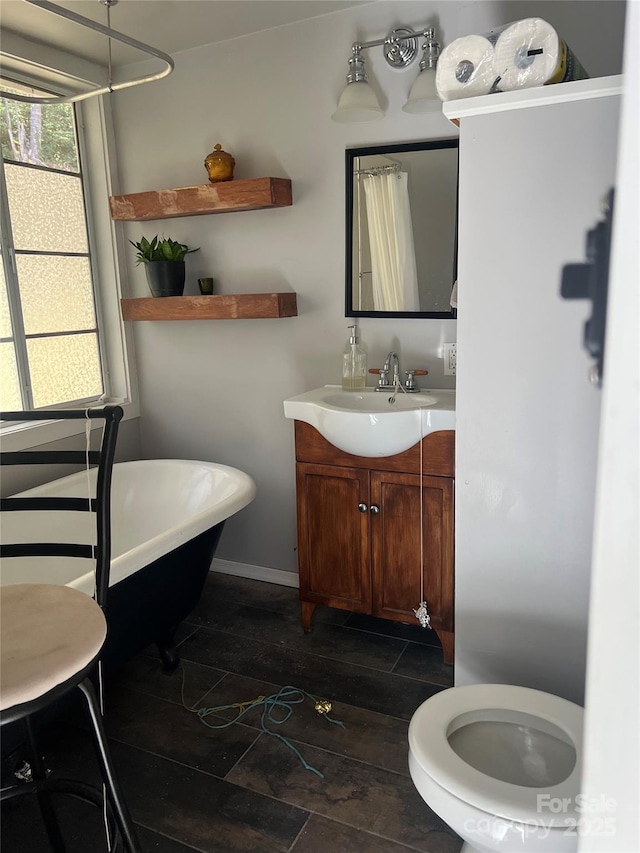 bathroom with toilet, a freestanding bath, vanity, and baseboards