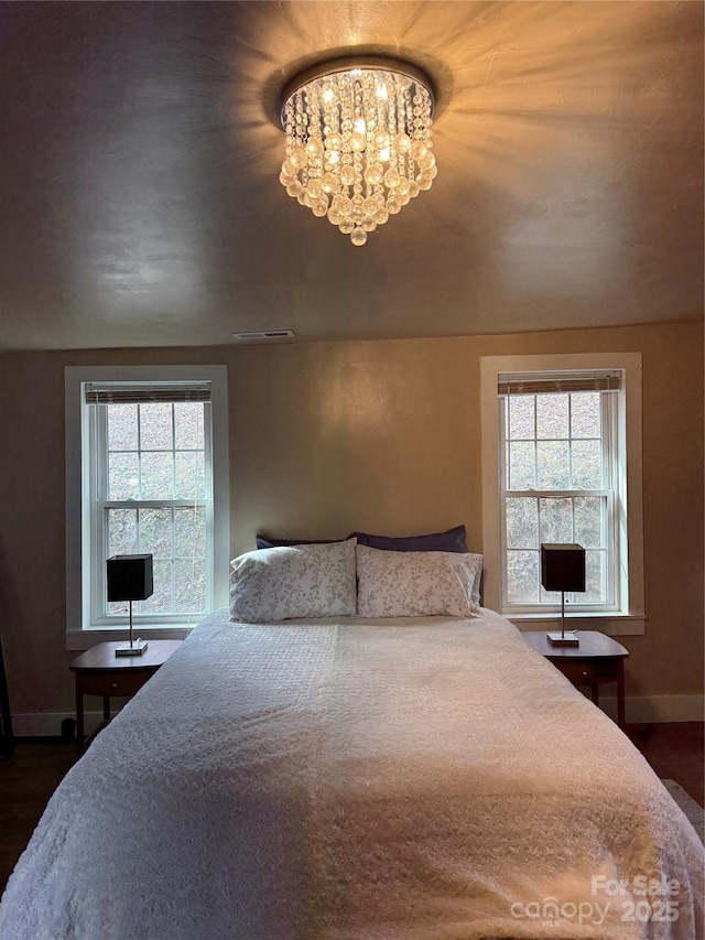 bedroom with dark wood finished floors, visible vents, a notable chandelier, and baseboards