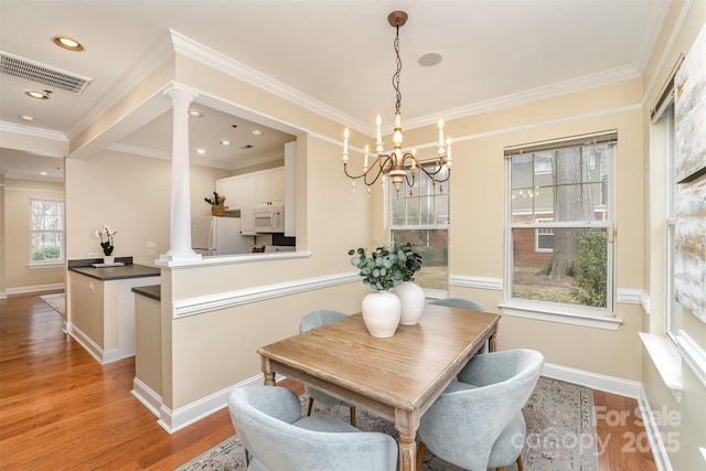 dining room with decorative columns, crown molding, and light hardwood / wood-style floors