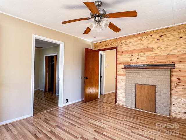 unfurnished living room featuring crown molding, ceiling fan, wood walls, and light wood-type flooring