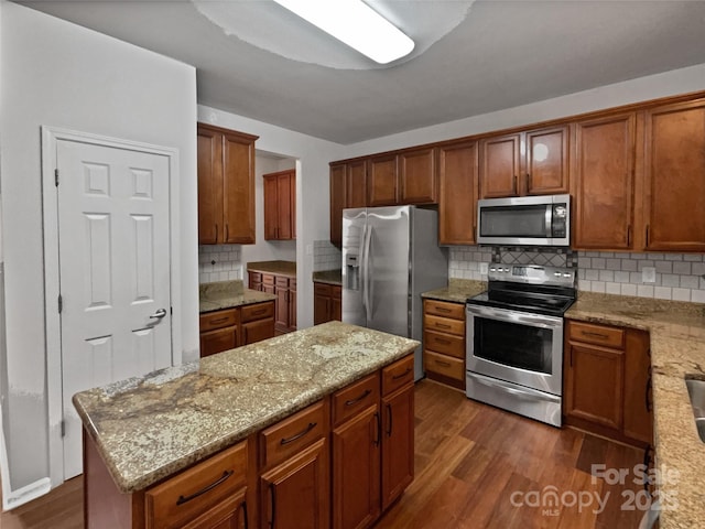 kitchen with tasteful backsplash, dark hardwood / wood-style flooring, a center island, light stone counters, and stainless steel appliances