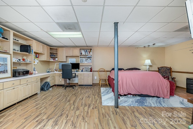 bedroom featuring a paneled ceiling, baseboards, built in desk, and light wood finished floors