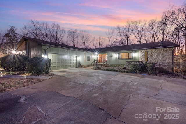 ranch-style home featuring driveway, stone siding, and an attached garage