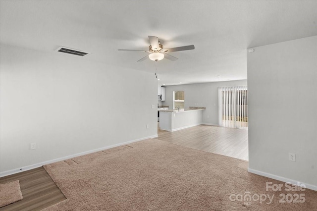 unfurnished living room featuring sink, light colored carpet, and ceiling fan