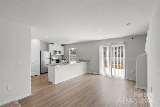 kitchen featuring appliances with stainless steel finishes, sink, white cabinets, light hardwood / wood-style floors, and kitchen peninsula