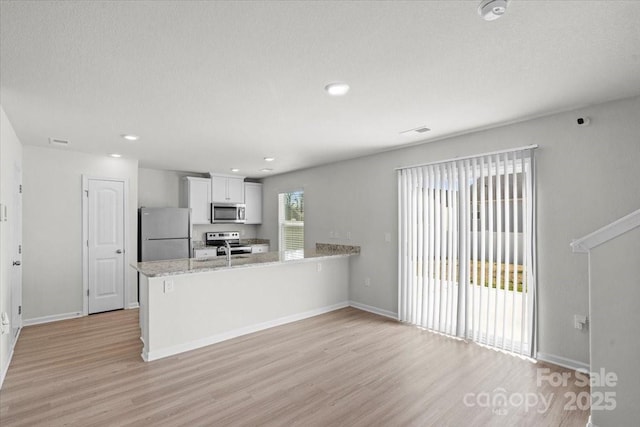 kitchen with white cabinetry, light stone counters, a textured ceiling, light wood-type flooring, and stainless steel appliances