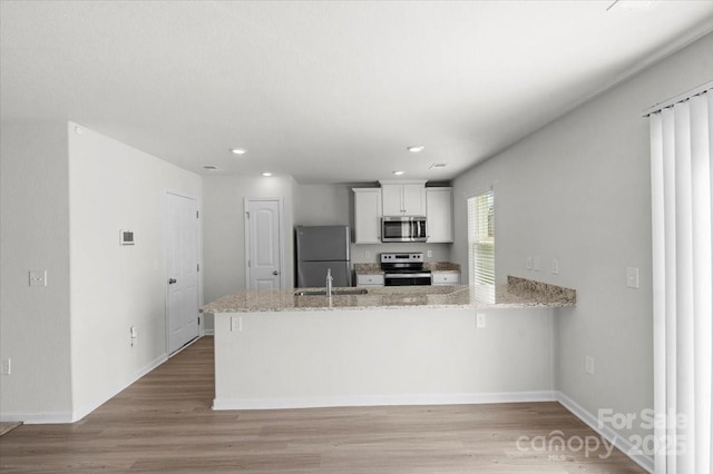 kitchen featuring sink, stainless steel appliances, light stone countertops, white cabinets, and kitchen peninsula