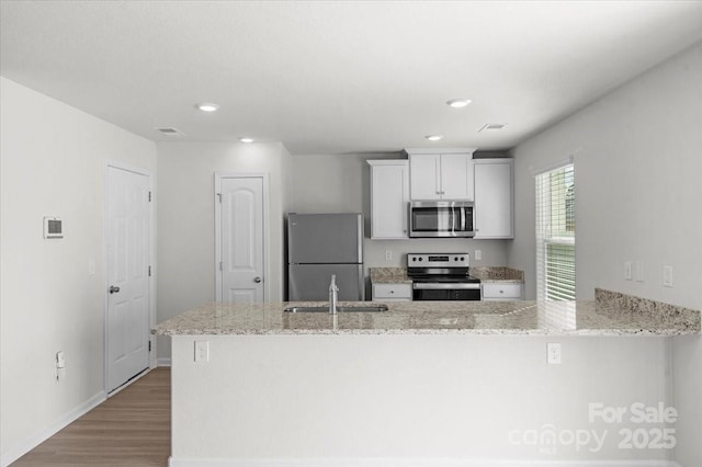 kitchen with white cabinetry, stainless steel appliances, light stone counters, wood-type flooring, and kitchen peninsula