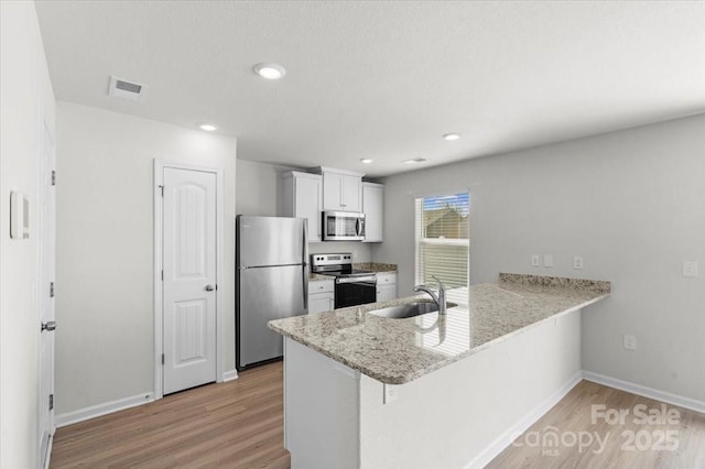 kitchen featuring sink, light hardwood / wood-style flooring, stainless steel appliances, white cabinets, and kitchen peninsula