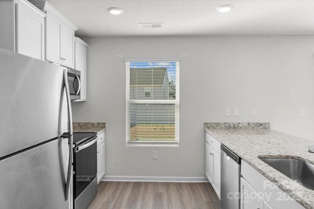 kitchen featuring sink, light stone counters, light wood-type flooring, appliances with stainless steel finishes, and white cabinets