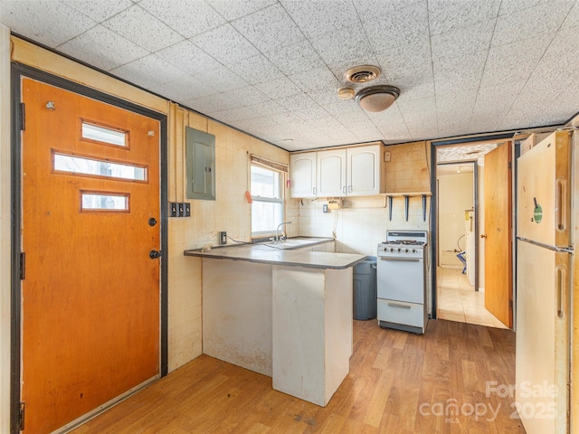 kitchen with kitchen peninsula, electric panel, white appliances, and light hardwood / wood-style flooring