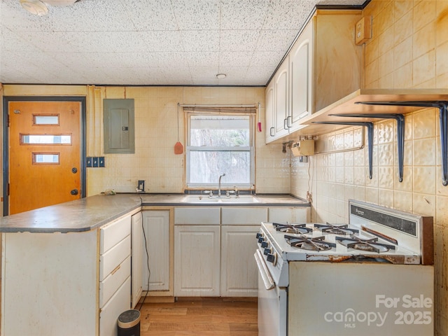 kitchen featuring white gas stove, sink, kitchen peninsula, electric panel, and backsplash