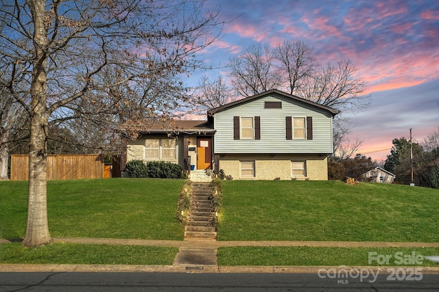 split level home featuring fence, a lawn, and brick siding