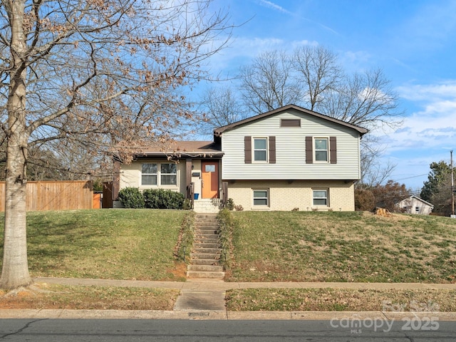 split level home with brick siding, a front yard, and fence