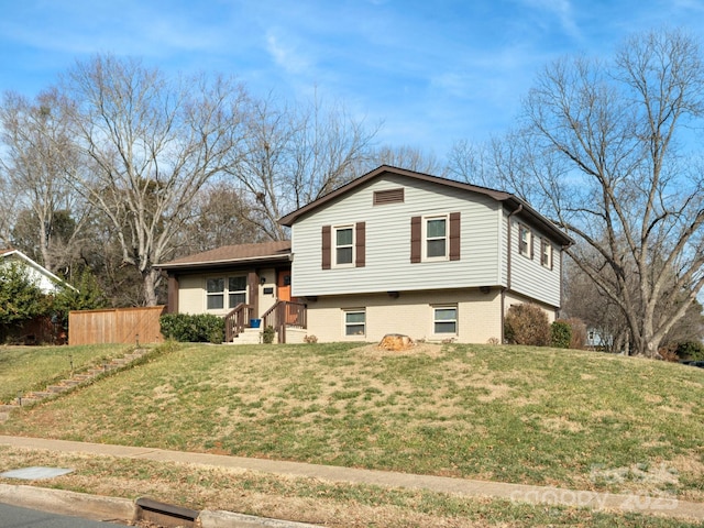 split level home featuring a front lawn, fence, and brick siding