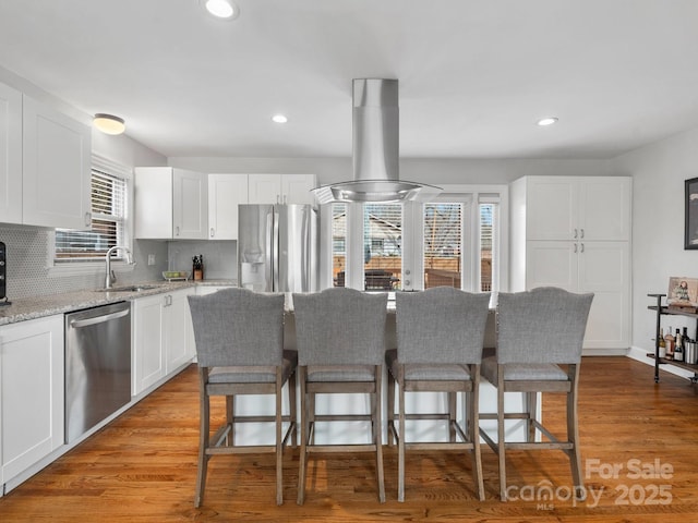 kitchen with light stone counters, appliances with stainless steel finishes, island exhaust hood, and white cabinetry