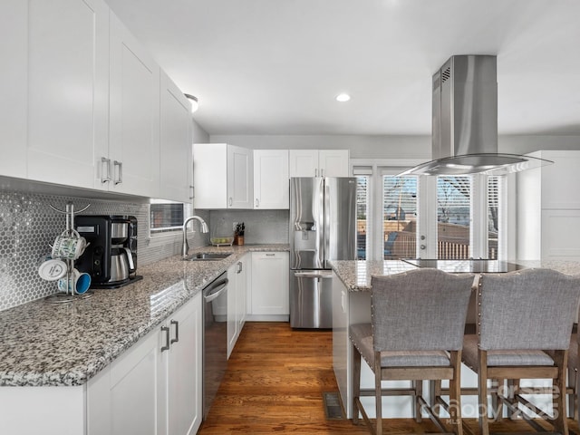 kitchen with light stone counters, stainless steel appliances, white cabinetry, a sink, and island range hood