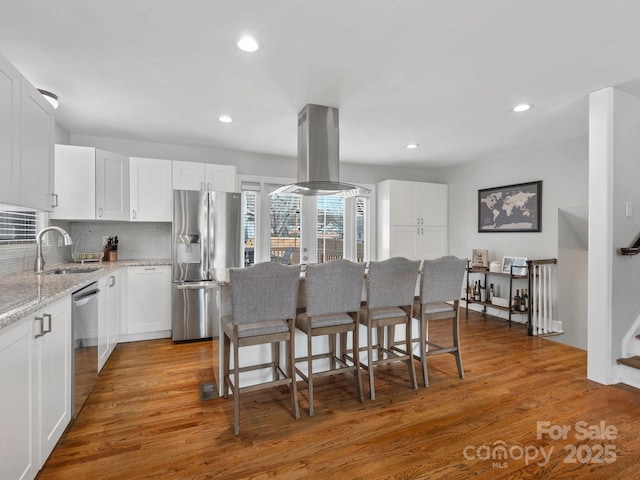 kitchen with appliances with stainless steel finishes, light wood-type flooring, island exhaust hood, and white cabinets