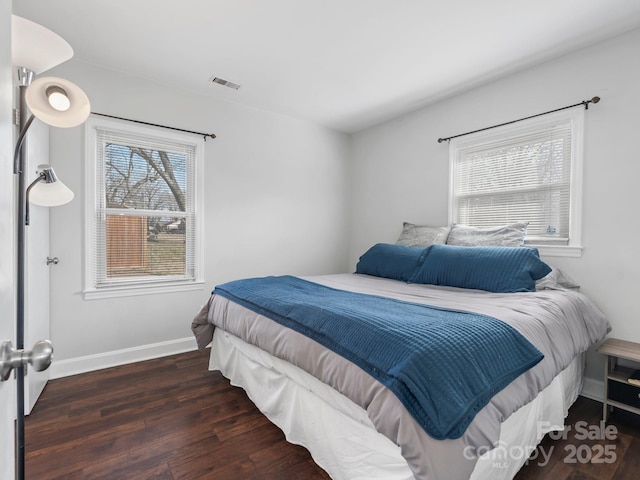 bedroom with dark wood-style flooring, multiple windows, visible vents, and baseboards