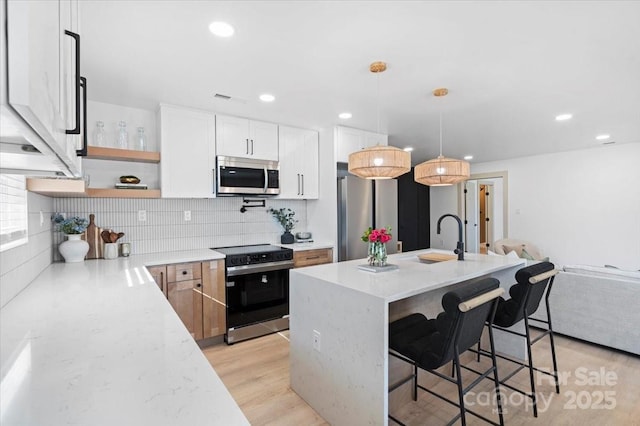 kitchen featuring appliances with stainless steel finishes, light stone countertops, white cabinets, a center island with sink, and decorative light fixtures