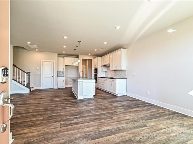 kitchen featuring sink, a kitchen island with sink, white cabinetry, decorative backsplash, and decorative light fixtures