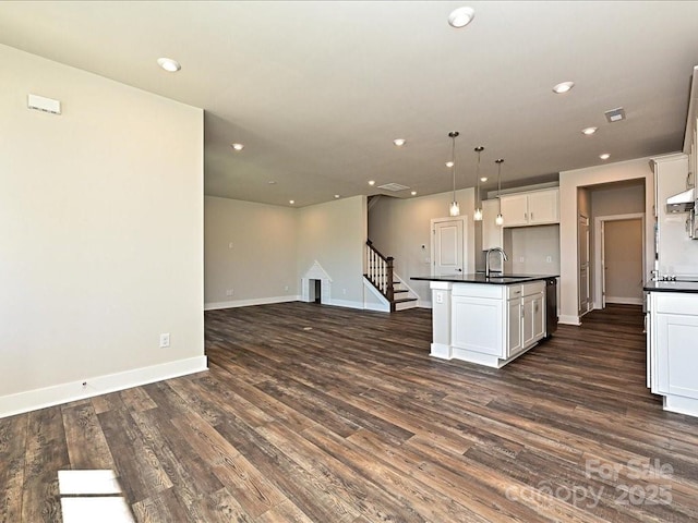 kitchen with dark hardwood / wood-style floors, white cabinetry, sink, hanging light fixtures, and a kitchen island with sink