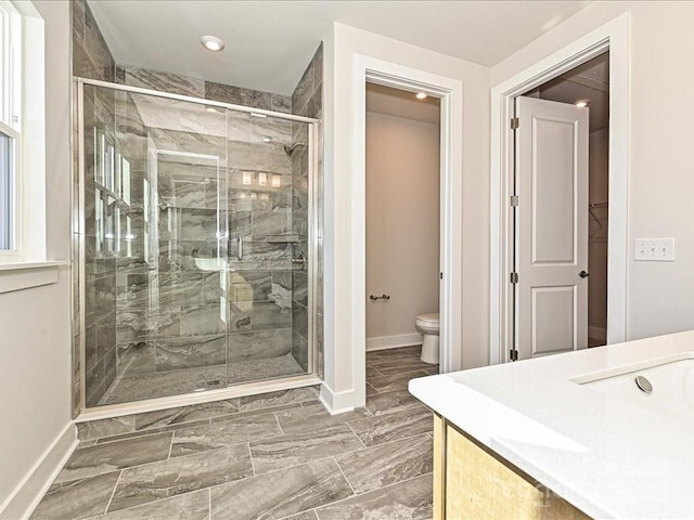 bathroom featuring a shower with door, vanity, and toilet